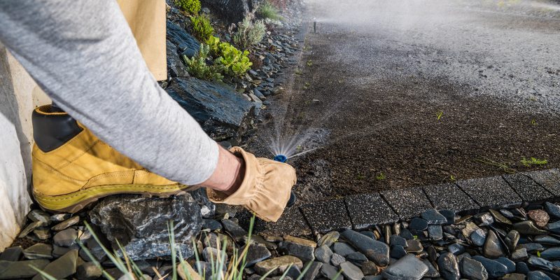 Landscaping Worker Adjusting Garden Water Sprinkler in a Newly Build Residential Backyard Garden. Modern Irrigation Systems. Gardening and Landscaping Theme.
